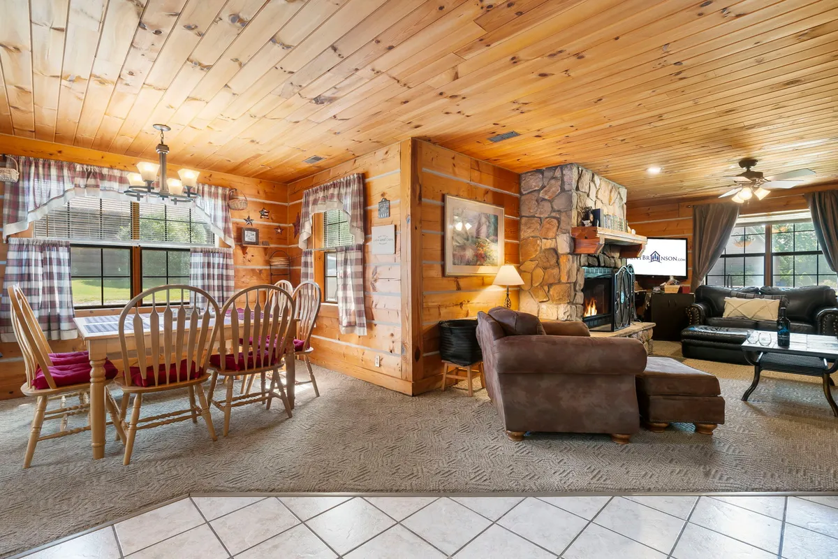 An interior shot showing a warm, inviting open-plan living space with a dining table, stone fireplace, comfortable seating area, and large windows letting in natural light. The room suggests homey comfort, space for family meals or group gatherings, and a cozy ambiance that aligns with the promise of a spotless, relaxing retreat.