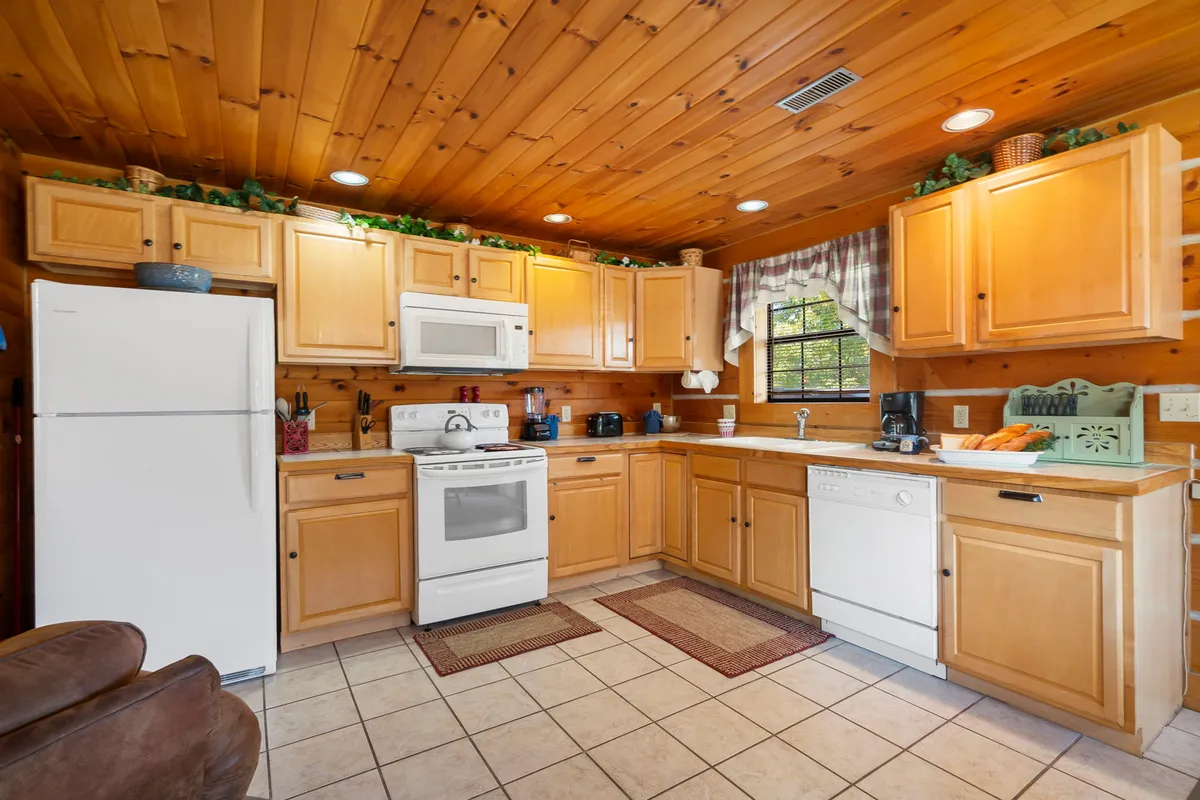 A cozy kitchen with natural wood cabinets, white appliances, and a window that lets in pleasant natural light. The space feels spacious and inviting, featuring plenty of countertop area for meal preparation, and evokes the warmth of family cooking and togetherness.