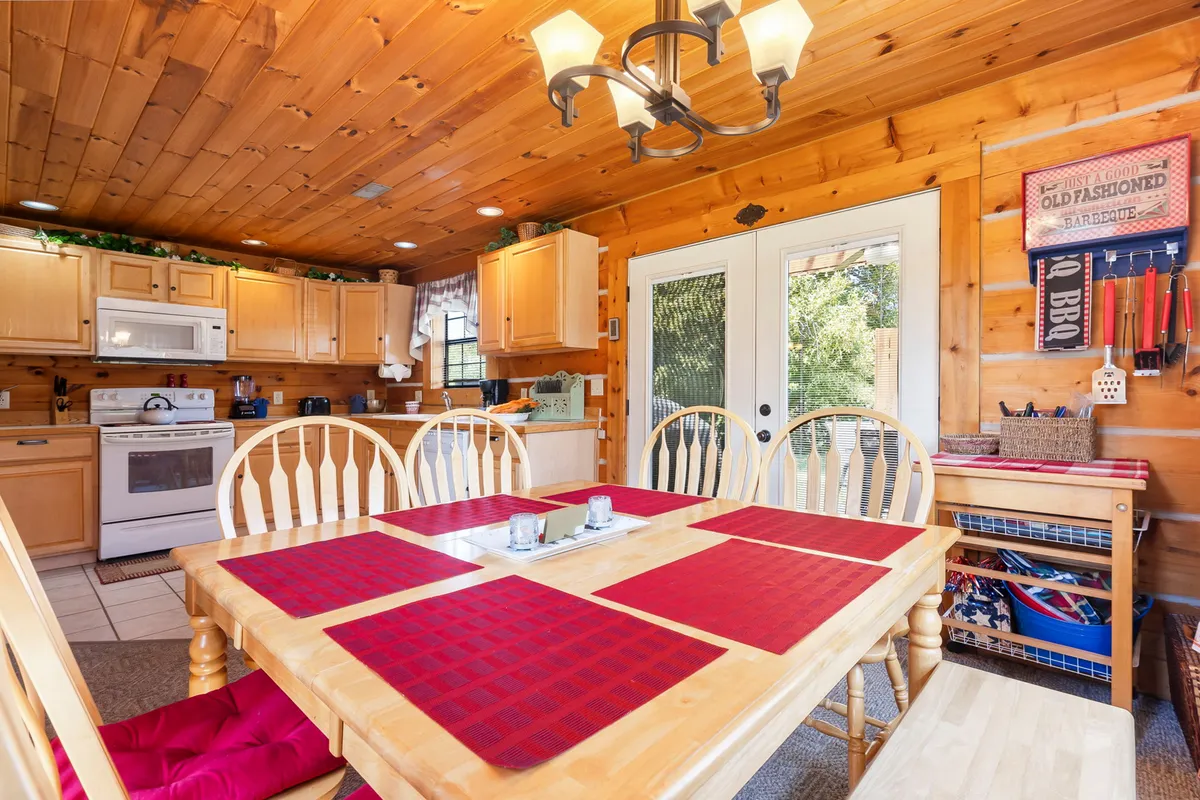 A dining area featuring a wooden dining table set with red placemats, surrounded by cabinetry and filled with natural light from large windows. The setting is ideal for family meals or casual gatherings, combining comfort and style.