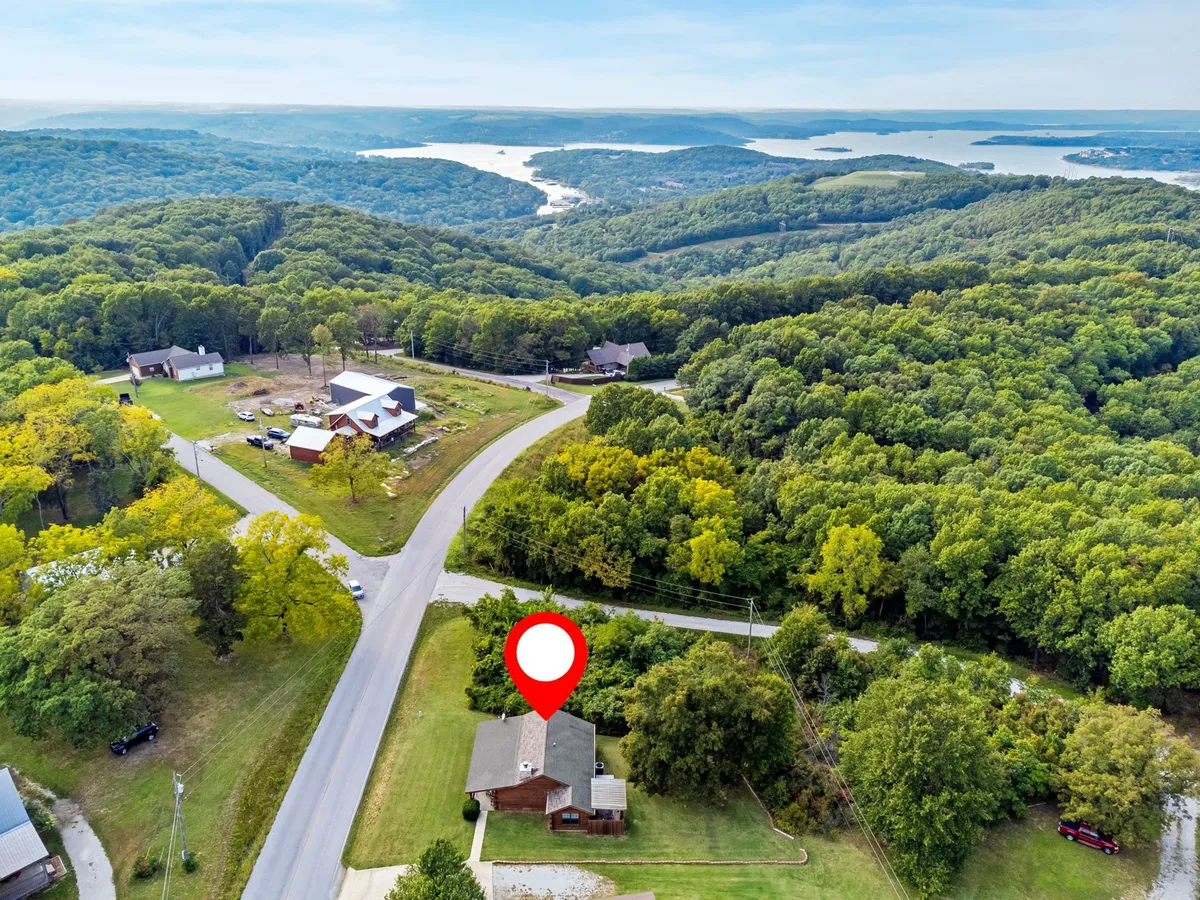 A peaceful home nestled among trees with a scenic lake view in the background. The surrounding natural beauty invites outdoor activities such as hiking, fishing, and lakeside recreation, all emblematic of the Ozarks experience.