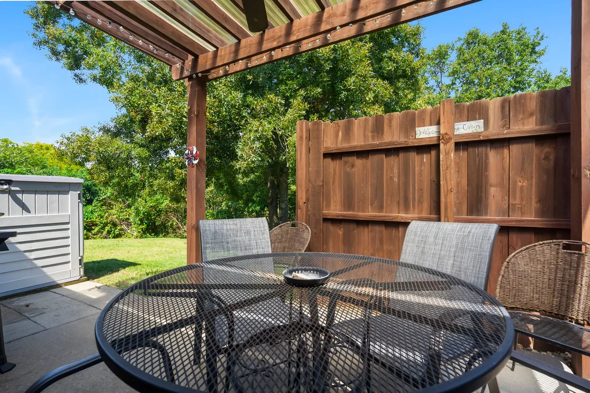 An inviting outdoor dining area with a round table and woven chairs set against a wooden fence, perfect for al fresco meals. The setup suggests intimate outdoor dining experiences, with enough seclusion and ambiance for couples to enjoy meals together amidst the sounds and sights of nature.