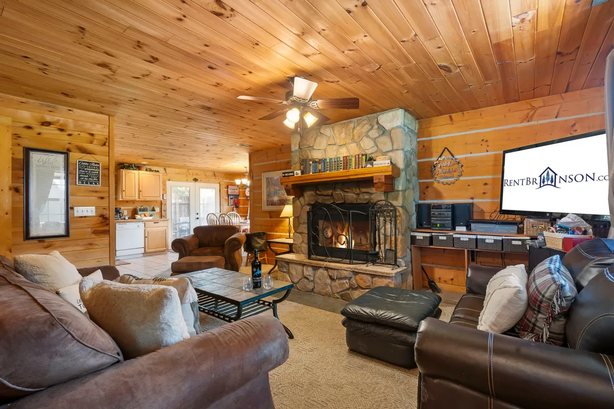 This cozy interior scene features a glowing wood-burning fireplace set against rustic wooden walls, with plush seating arranged for comfort. A TV is mounted nearby, inviting guests to enjoy movie nights, while the warm lighting and inviting furnishings create a homely atmosphere perfect for relaxing after outdoor adventures.