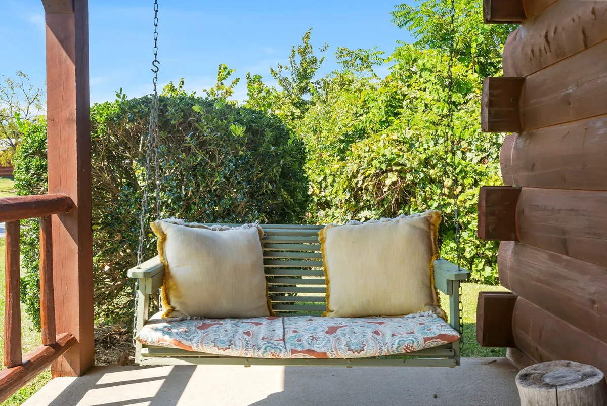 A serene exterior scene focused on a swing bench with decorative pillows surrounded by lush greenery. The mood is calm and inviting, suggesting peaceful moments spent relaxing outdoors after a day’s activities.