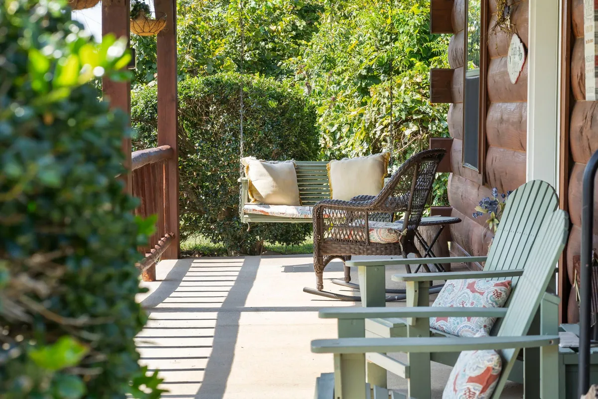 A charming porch setup with a swing bench, cushioned wicker and wooden chairs, all overlooking lush greenery. The space feels tranquil and is ideal for relaxing after a day outdoors with your furry companion.