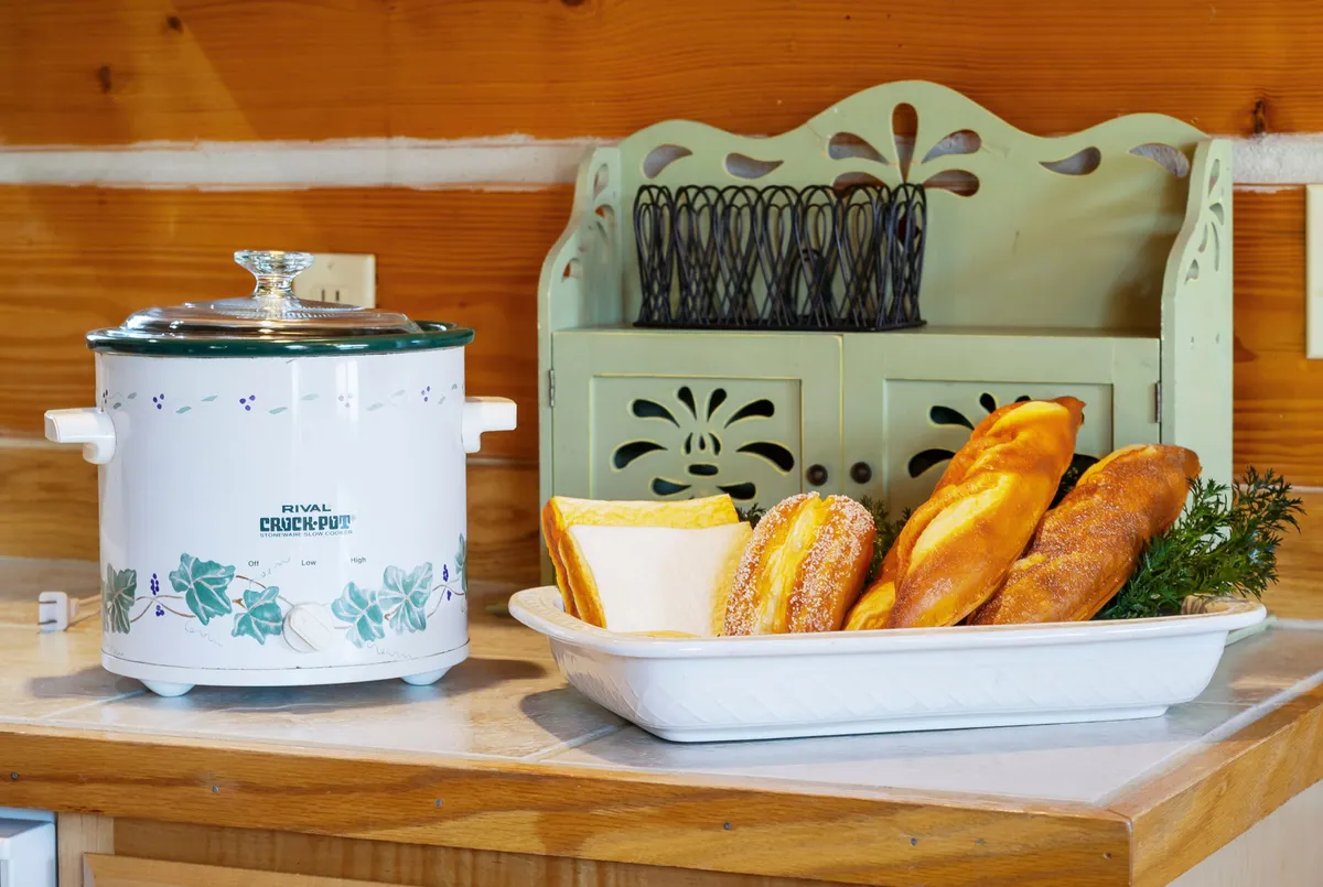 A tray of fresh baked goods and a crock pot are displayed on a decorative shelf, creating a warm atmosphere that hints at home-cooked meals and cozy gatherings. The setting suggests the joy of creating and sharing food as a group.