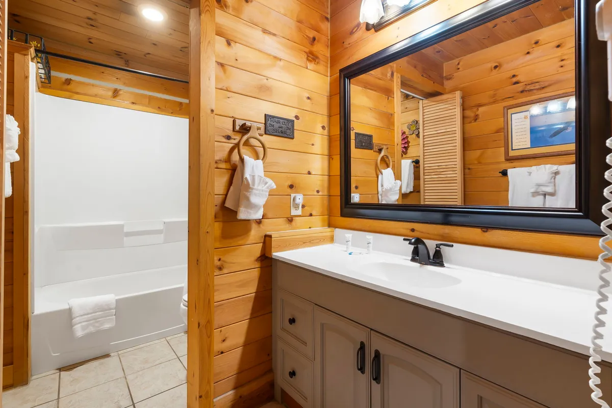 A well-appointed hallway bathroom featuring wooden paneling, a large mirror, and a white sink. The space feels serene and functional, ready to accommodate the needs of all guests.