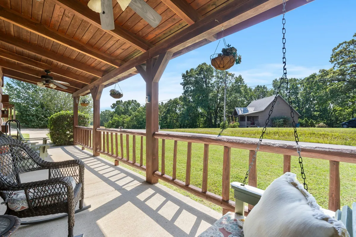 A charming exterior porch scene featuring classic wooden rocking chairs, hanging plants, sturdy wooden beams, and lush greenery. The porch exudes a sense of welcoming tranquility and is bathed in soft natural light, making it an inviting spot for couples to enjoy their mornings or evenings together.