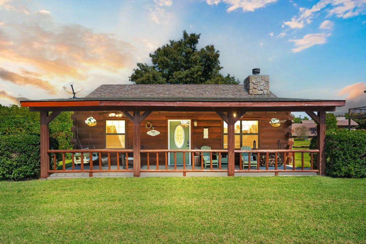 This image features a classic wooden cabin structure with a welcoming front porch furnished with rocking chairs, set against a green lawn. The scene exudes rustic charm and an inviting atmosphere, capturing the essence of a private log cabin retreat. The porch and natural surroundings emphasize opportunities for relaxation and connection with nature.